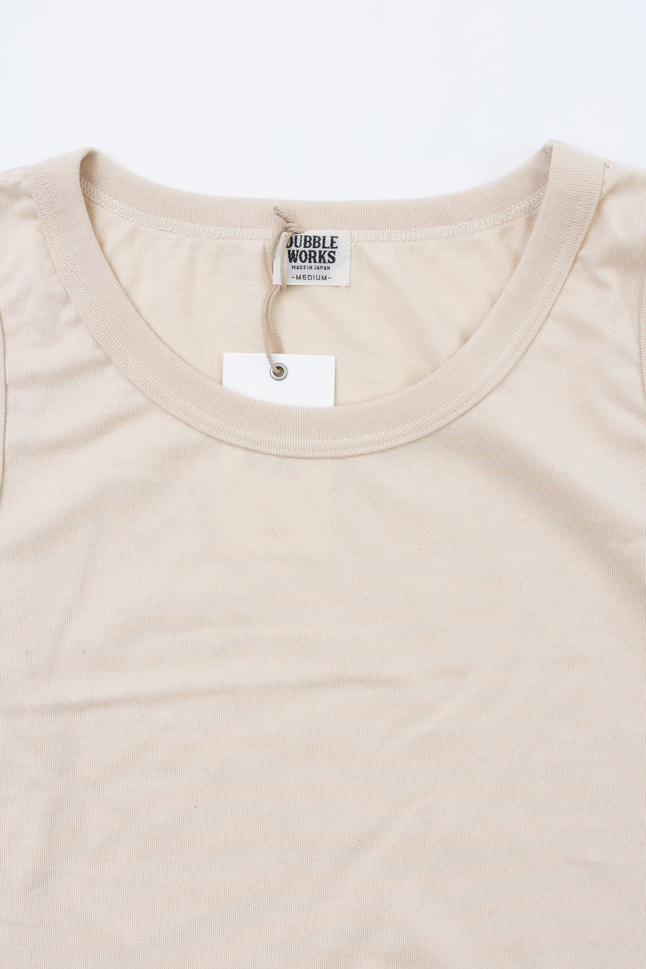 Close-up of beige t-shirt collar with BUBBLE WORKS tag, showing front neckline and fabric texture