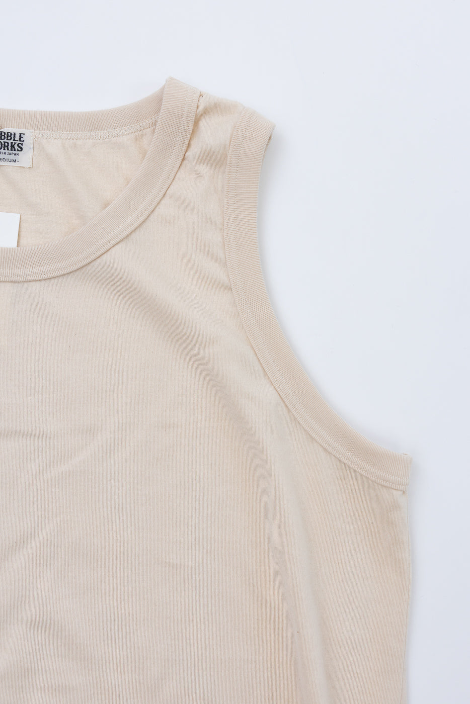 Close-up front view of beige ribbed tank top showing crew neck, sleeve hem, and tag detail