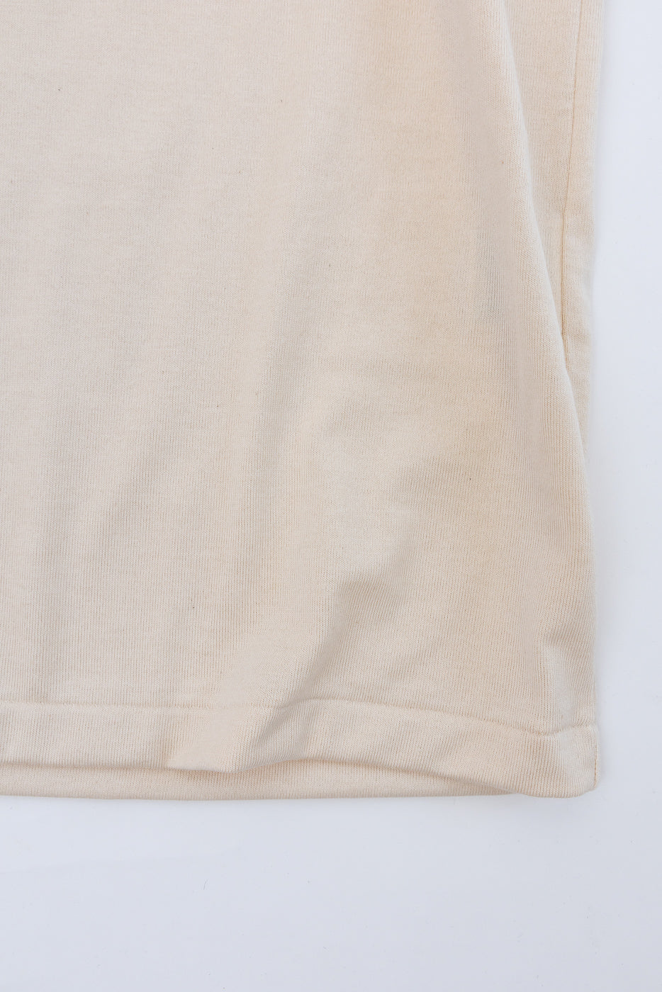 Close-up of beige t-shirt hem, front view, showing ribbed knit texture and clean stitching detail