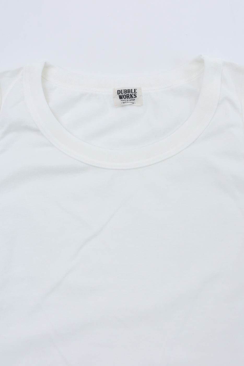Close-up of white t-shirt collar with Dubble Works tag, front view, soft fabric texture