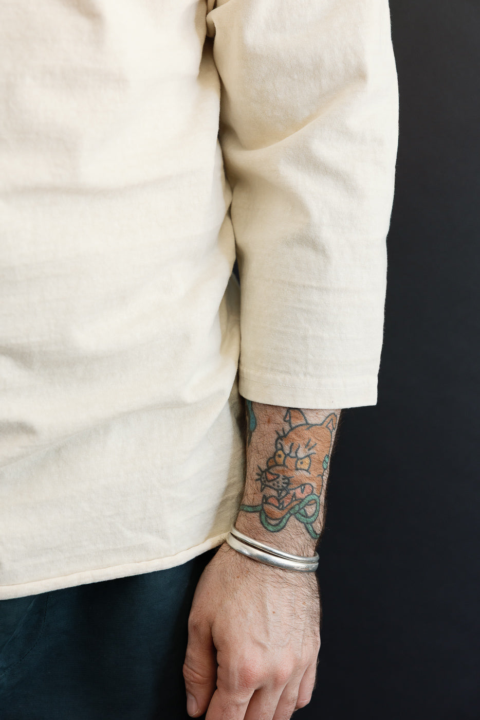 Close-up of male model's arm in cream shirt, showing sleeve hem and tattoo, athletic build