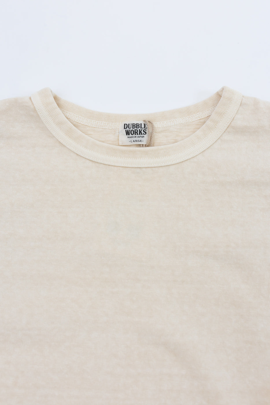 Close-up front view of cream crew neck tee, showing Dubble Works tag, ribbed collar, and soft cotton texture