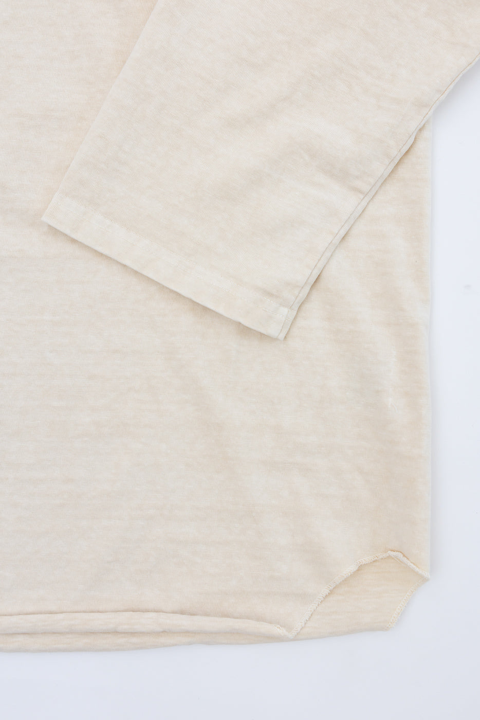 Close-up of beige long-sleeve shirt hem and sleeve cuff, showcasing soft fabric texture and clean stitching.