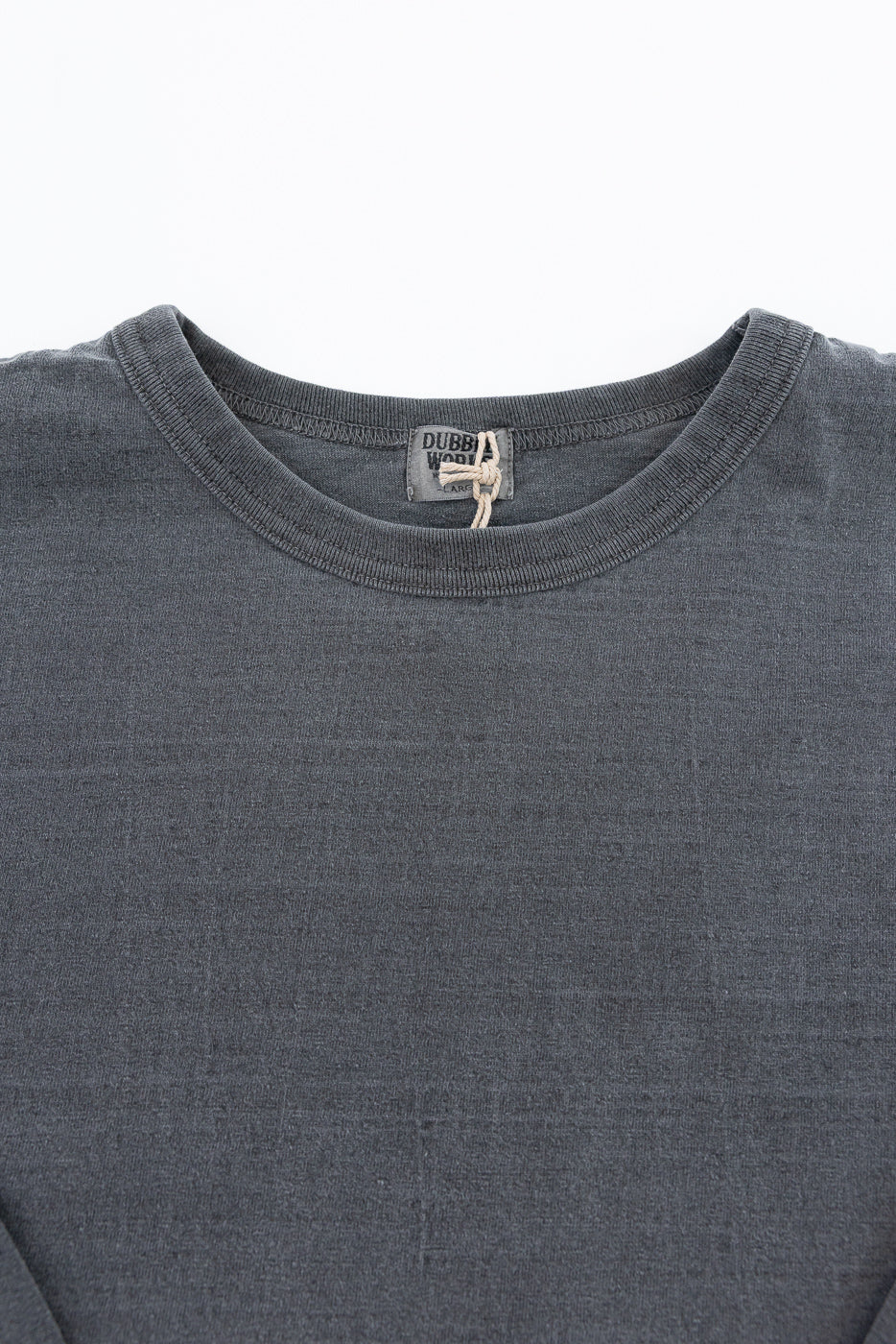 Close-up front view of dark gray long-sleeve tee, showing ribbed crew neck, fabric texture, and brand tag with twine tie.