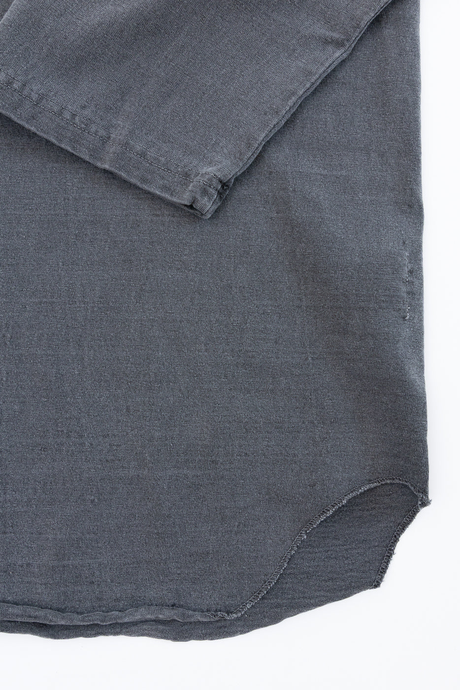 Close-up of dark gray shirt hem, showing curved raw edge and fabric texture, front view