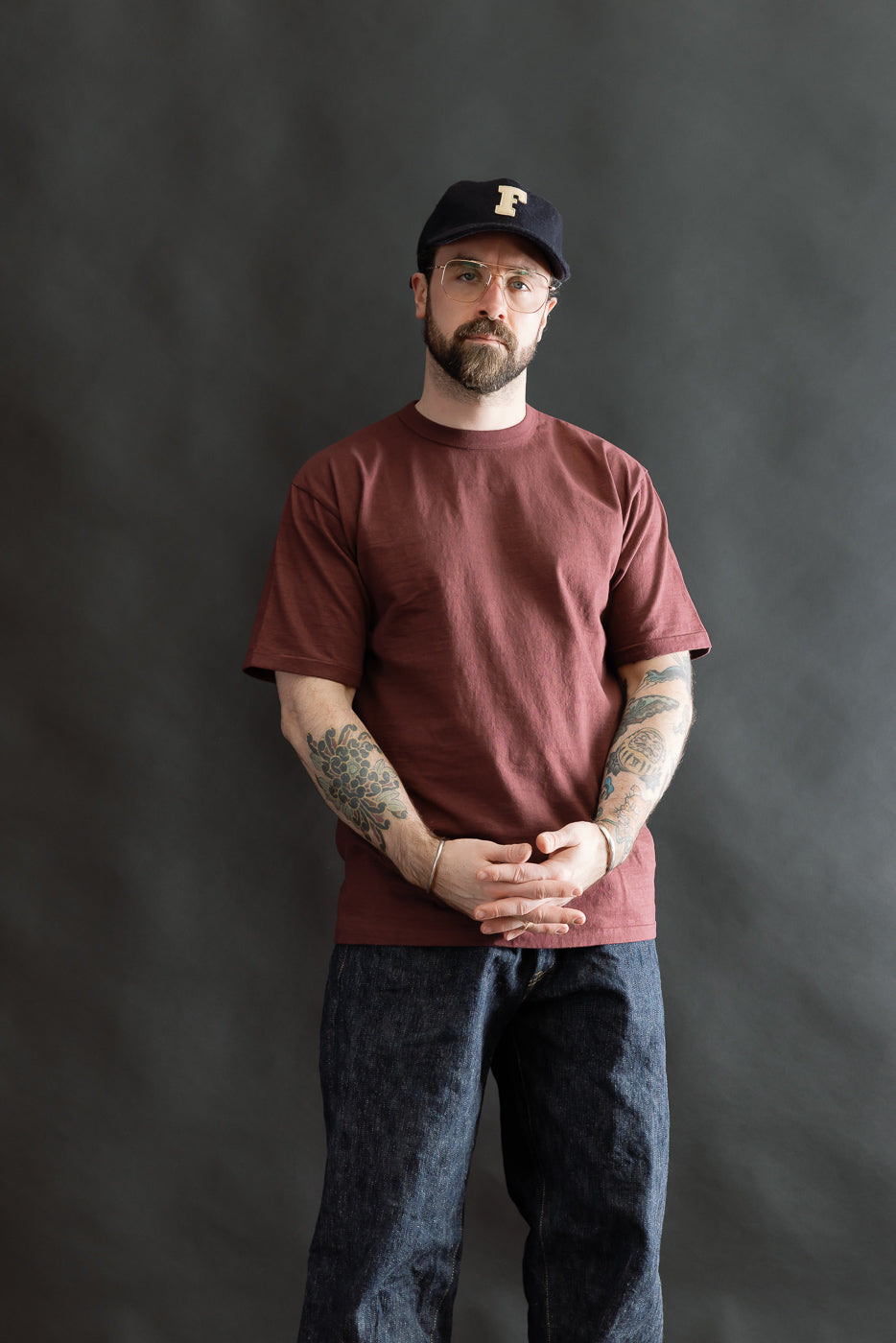 Man wearing a Fallen Cotton Midweight T-Shirt S/S - Bordeaux, styled with straight-leg blue jeans. The shirt's recycled cotton slub jersey showcases a natural texture, embodying Dant's heritage-inspired menswear aesthetic.
