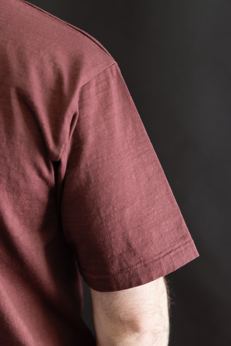 Close-up of a person's upper arm wearing the 7.7oz Fallen Cotton Midweight T-Shirt S/S - Bordeaux, showcasing the textured recycled cotton slub fabric and classic short sleeve design.