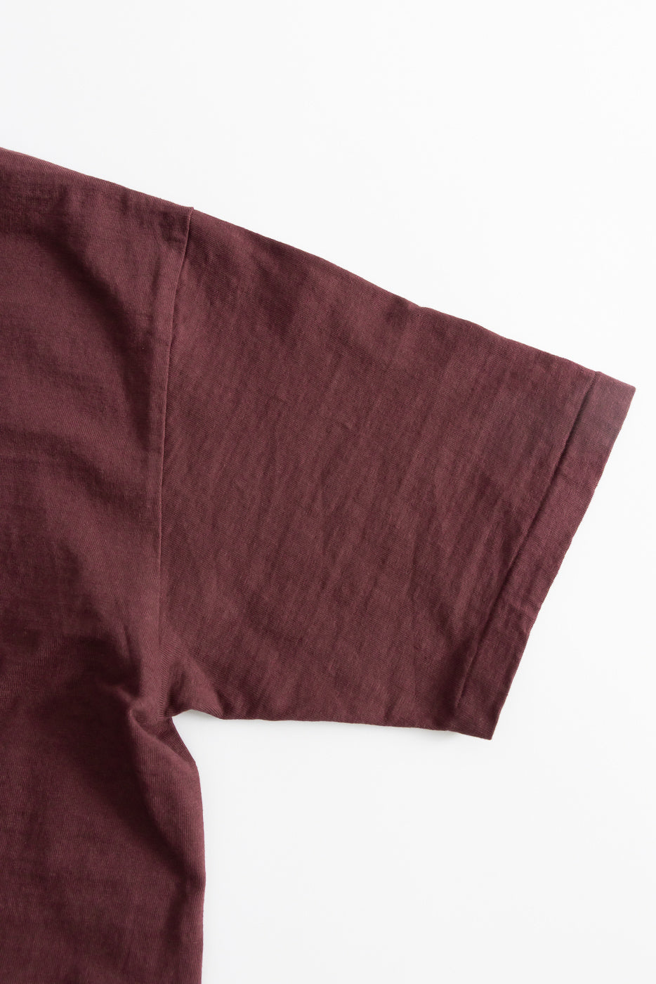 Close-up of the 7.7oz Fallen Cotton Midweight T-Shirt S/S in Bordeaux, showcasing the short sleeve and seam detail of the recycled cotton slub jersey, highlighting its textured and soft fabric.