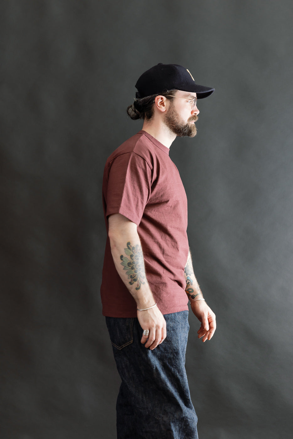 Bearded man in a 7.7oz - Fallen Cotton Midweight T-Shirt S/S - Bordeaux, showcasing the tee's soft, textured fabric and classic silhouette, ideal for layering and everyday comfort, styled with denim jeans.
