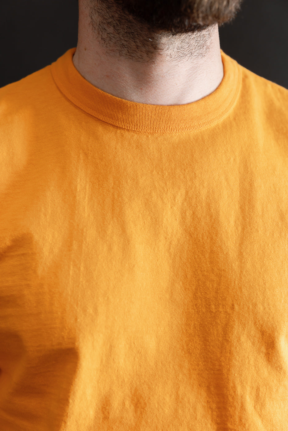 Close-up of a model wearing the 7.7oz - Fallen Cotton Midweight T-Shirt S/S in Fade Orange, showcasing the textured recycled cotton slub jersey and classic crew neck design.