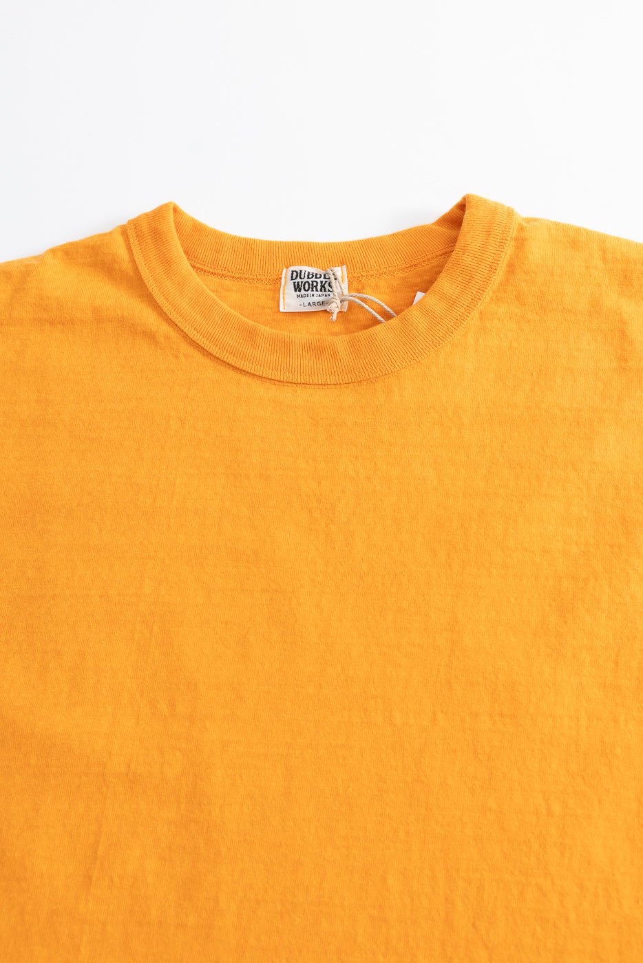 7.7oz Fallen Cotton Midweight T-Shirt S/S in Fade Orange laid flat, highlighting its recycled cotton slub jersey texture with a factory label reading DUBBLE WORKS – MADE IN JAPAN – LARGE.