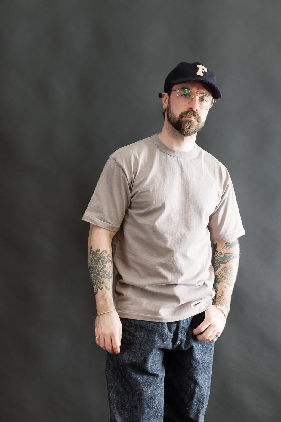 Man wearing a Fallen Cotton Midweight T-Shirt S/S - Grey, showcasing its natural slub texture and casual fit, paired with dark denim jeans, illustrating a relaxed, heritage-inspired style.