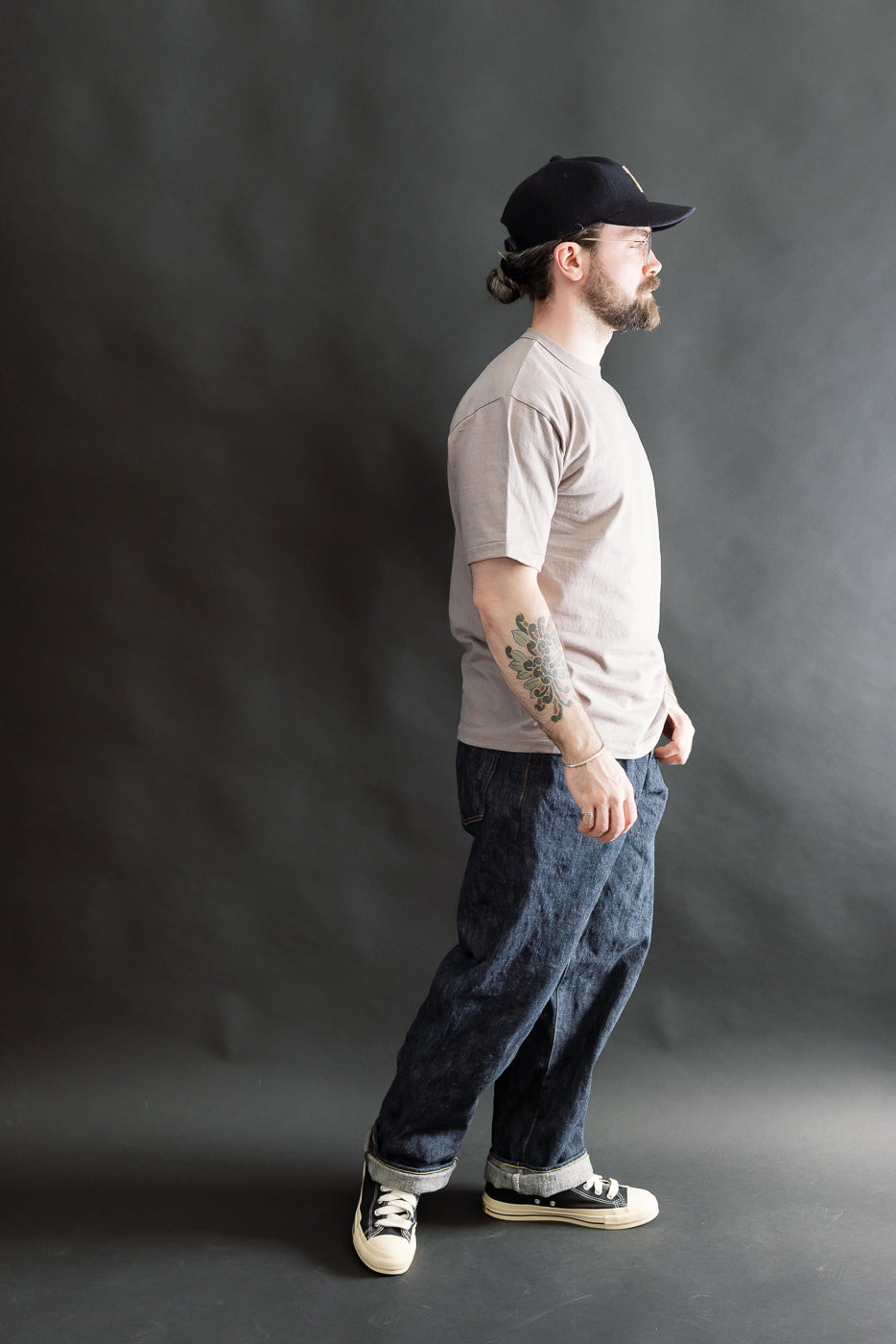 A man in profile wears the 7.7oz Fallen Cotton Midweight T-Shirt S/S - Grey, styled with dark jeans and black sneakers, embodying a minimalist and casual look.