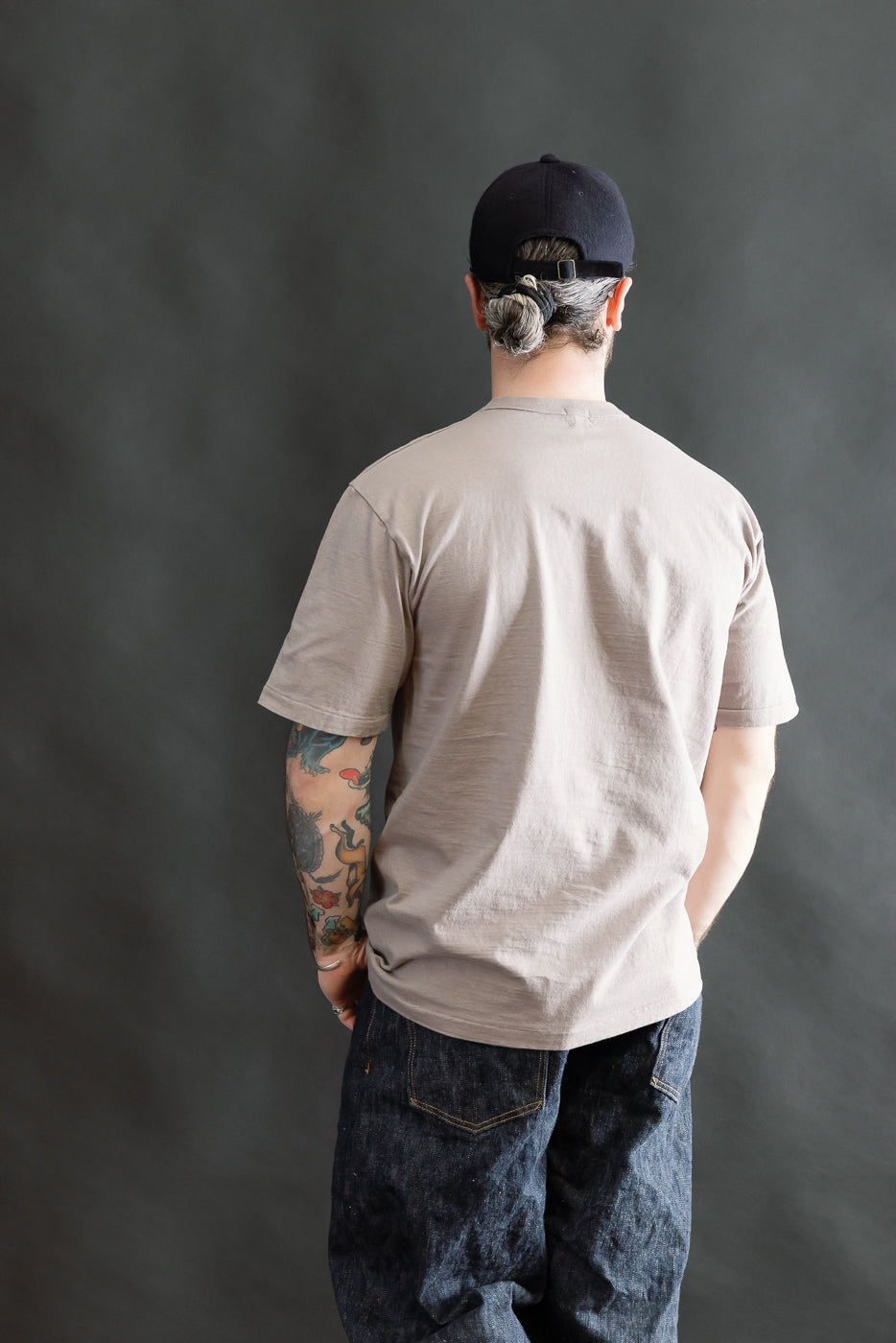 The image shows a man wearing the 7.7oz Fallen Cotton Midweight T-Shirt S/S in Grey, highlighting its casual fit, textured slub jersey, and classic tee construction with a round body and short sleeves.