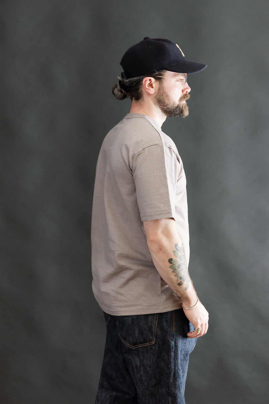 Bearded man in profile wears the 7.7oz Fallen Cotton Midweight T-Shirt S/S - Grey, showcasing its recycled cotton slub texture, short sleeves, and round body design.