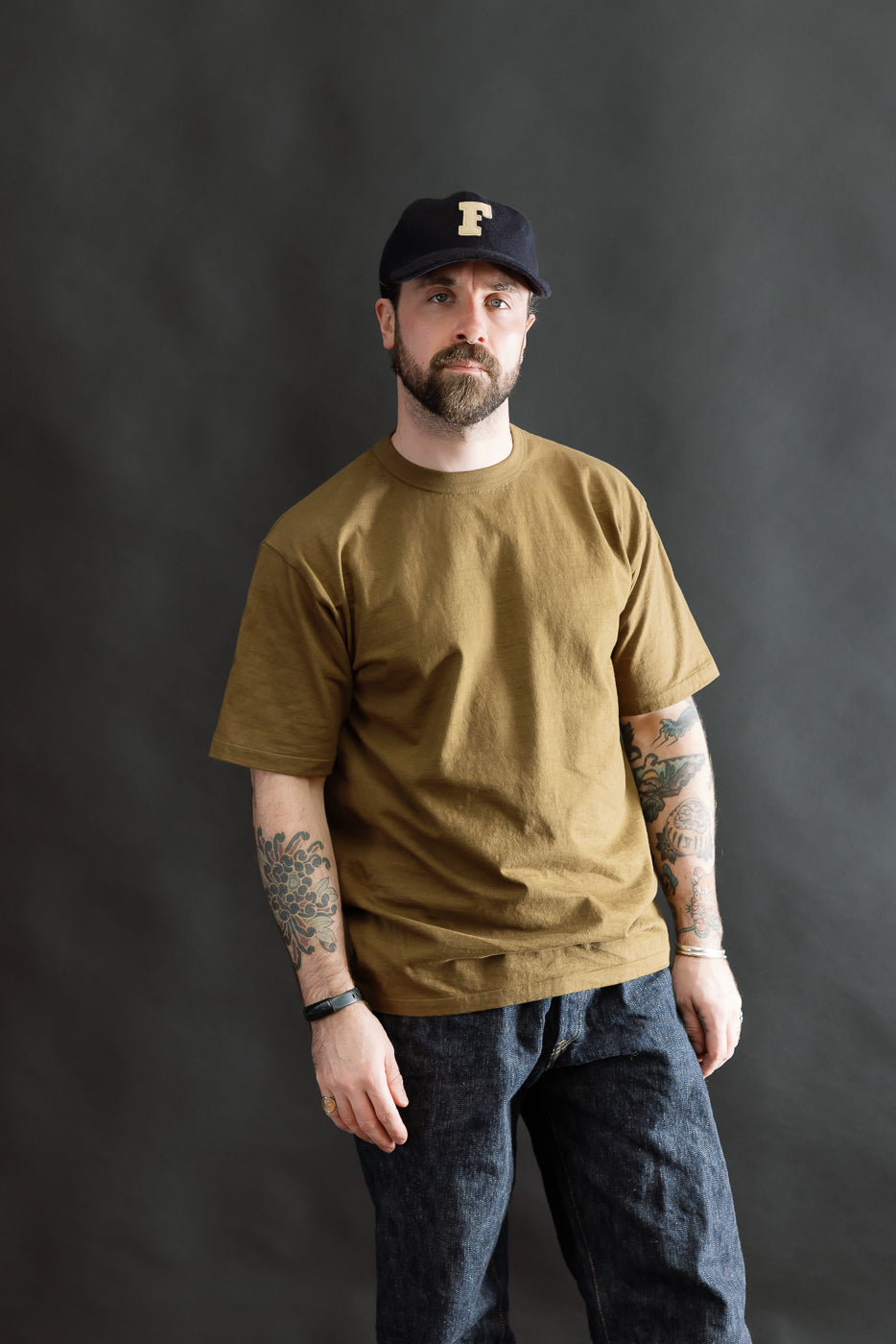 Model wearing the 7.7oz Fallen Cotton Midweight T-Shirt S/S - Khaki, showcasing its fit and texture. The tee features a round body and single-stitched hem, ideal for layering and everyday wear.