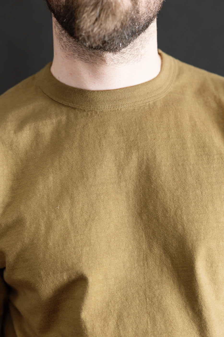 Close-up of a man's lower face and upper torso wearing the 7.7oz - Fallen Cotton Midweight T-Shirt S/S - Khaki, showcasing its textured recycled cotton slub jersey and clean, classic crew-neck design.