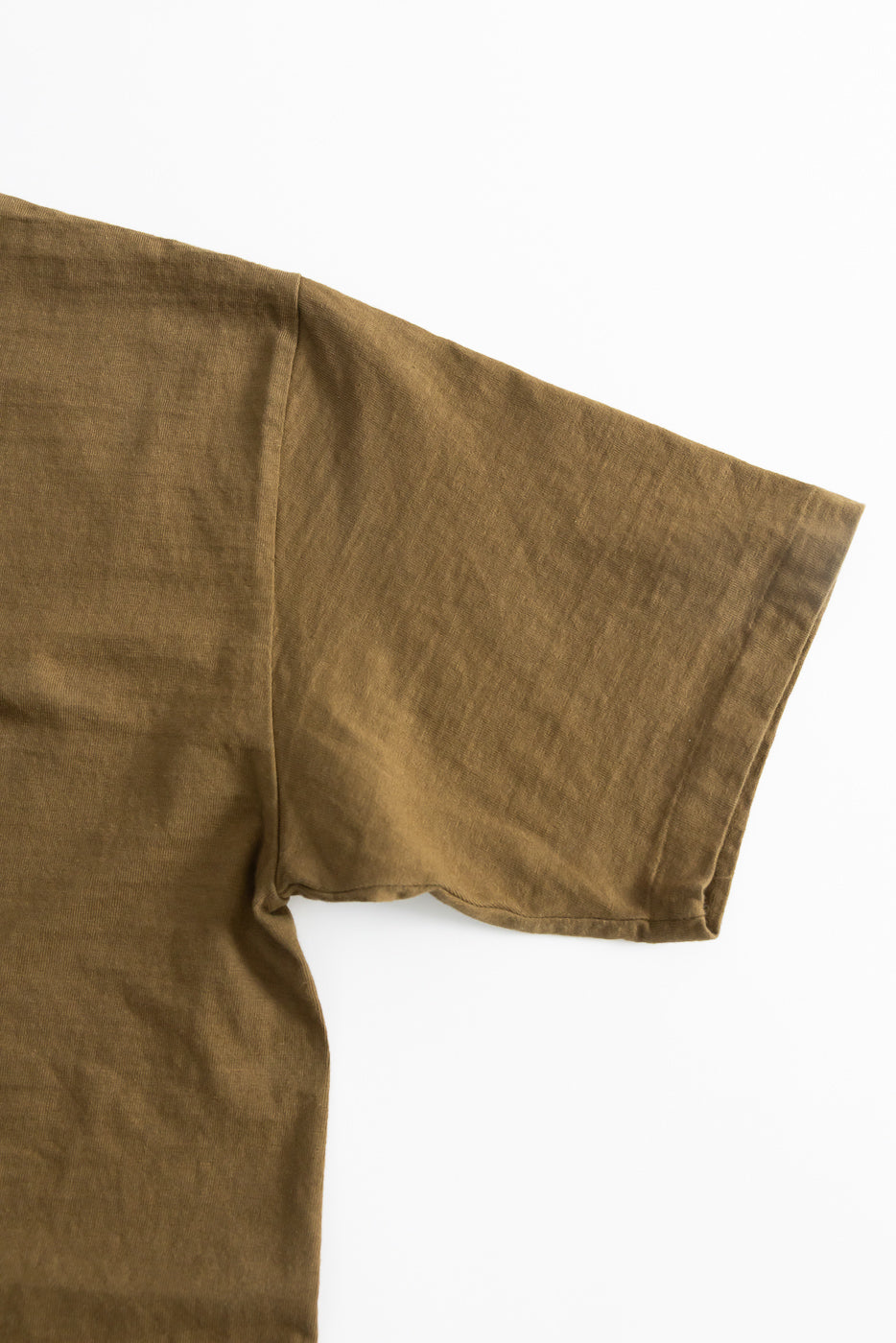 Close-up of the short sleeve and shoulder of the 7.7oz Fallen Cotton Midweight T-Shirt S/S - Khaki, showcasing recycled cotton slub jersey's natural uneven texture and single-stitched hem against a white background.
