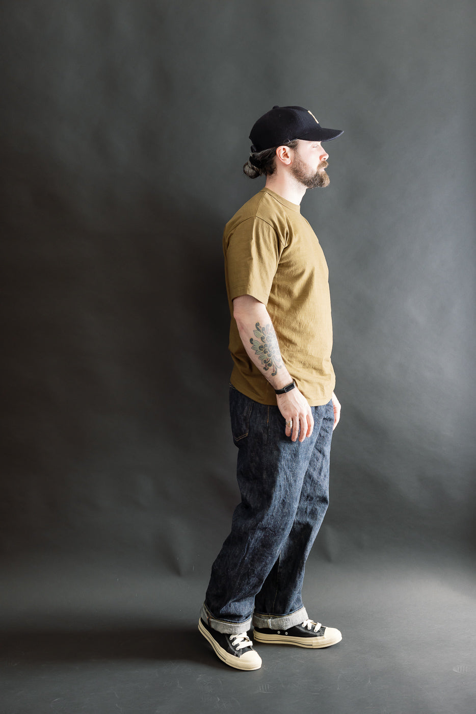 Man in profile wearing the 7.7oz Fallen Cotton Midweight T-Shirt S/S - Khaki. Features include a round body, binder neck, and single-stitched hem, highlighting its natural uneven slub texture.