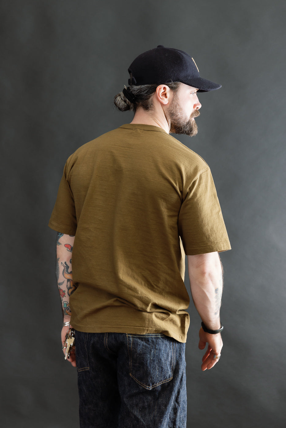Model displays the 7.7oz Fallen Cotton Midweight T-Shirt S/S in Khaki. He stands slightly turned, showcasing the tee's fit, recycled cotton slub texture, and classic round body design.