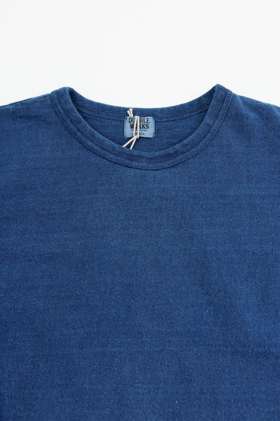 Close-up front of indigo blue crewneck tee, showing ribbed collar and Double Works tag, soft cotton texture