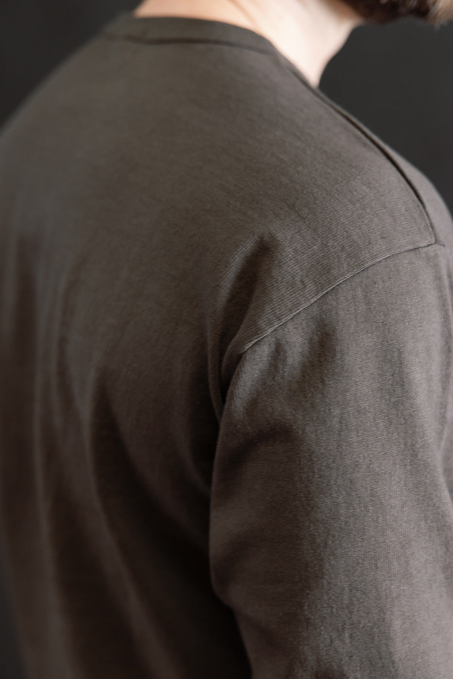 Close-up of male model's upper back and shoulder in sumikuro heavyweight long sleeve tee, side view, showing fabric texture and seam detail. Model is 5'9