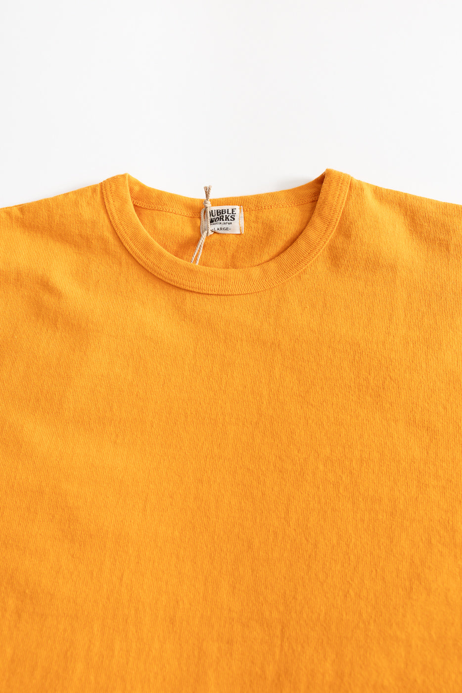 Close-up of front upper section of heavyweight fade orange tee, showing crew neck, tag, and fabric texture.
