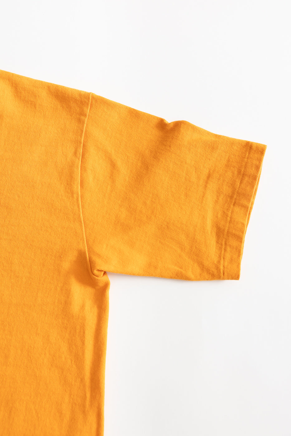 Close-up of fade orange heavyweight tee, flat lay, showing left sleeve and front side texture.