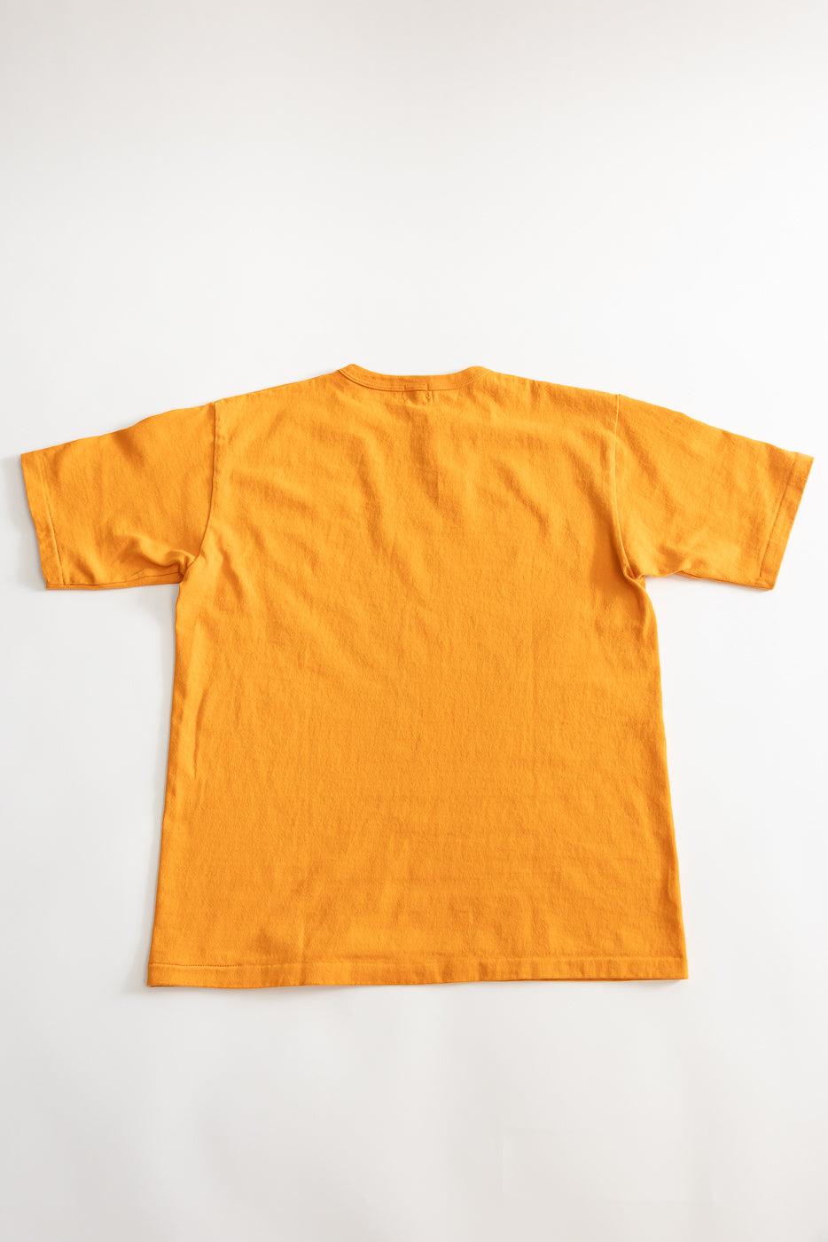 Flat lay of heavyweight fade orange tee, back view, showing short sleeves and hem detail.