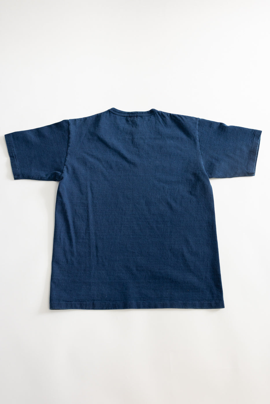 Flat lay of indigo dyed heavyweight tee, back view showing short sleeves and straight hem.