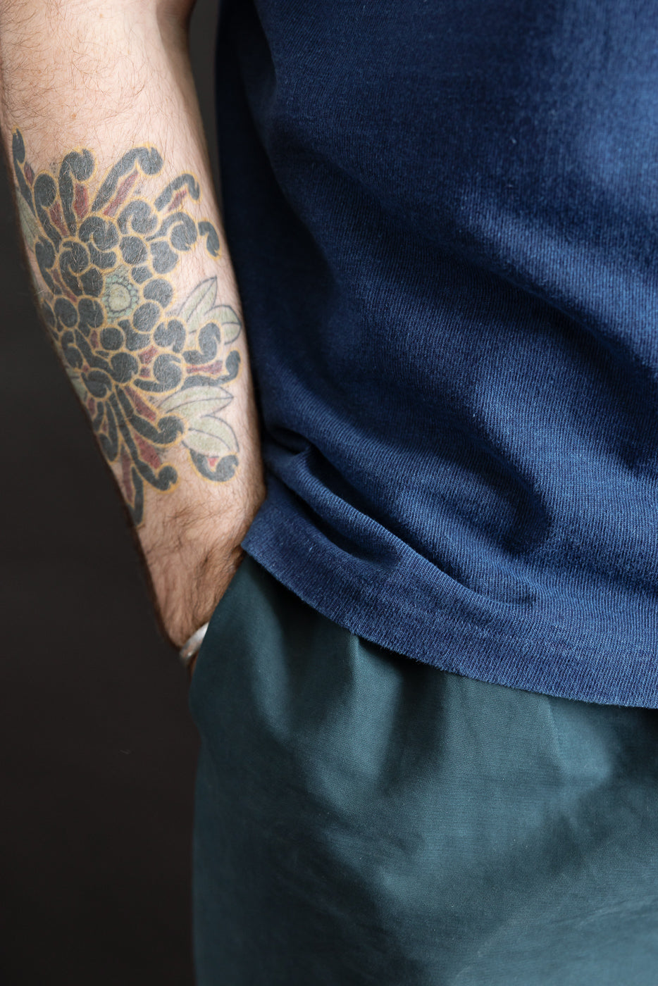 Close-up of indigo dyed heavyweight tee hem, side view on male model 5'9 165lbs athletic build, showing fabric texture.