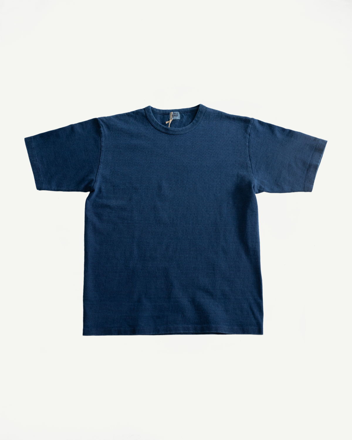 Flat lay of front of indigo-dyed heavyweight tee, short sleeves, crew neck, visible fabric texture.