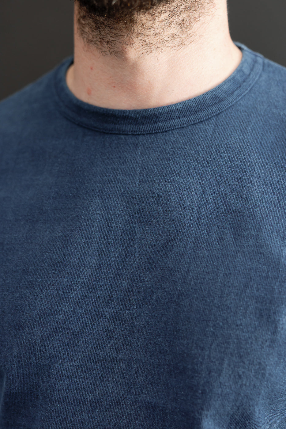 Close-up front view of a male model's neck and crewneck collar on a navy blue textured tee.