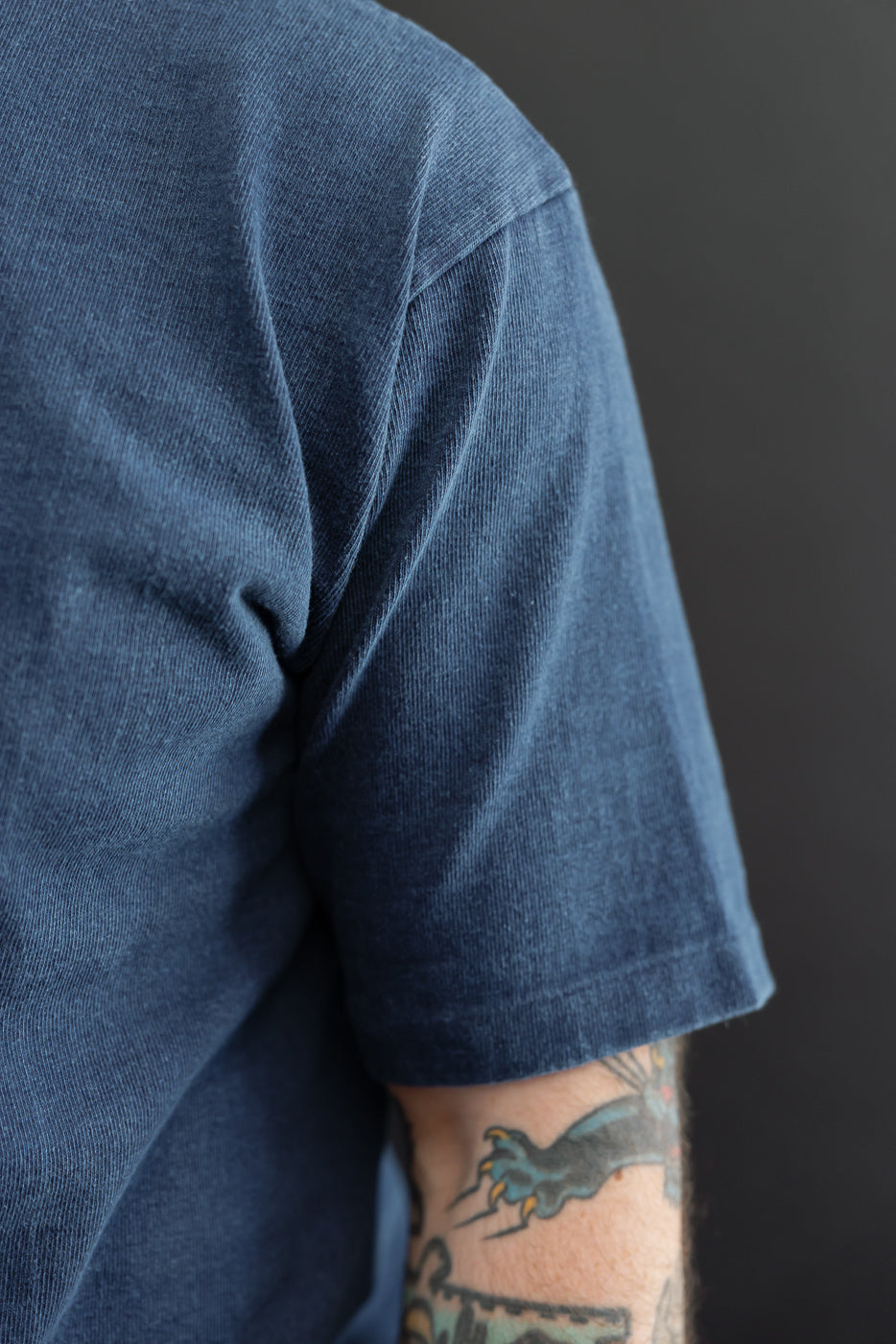 Close-up side view of male model's arm in blue corduroy tee, showing sleeve hem and fabric texture