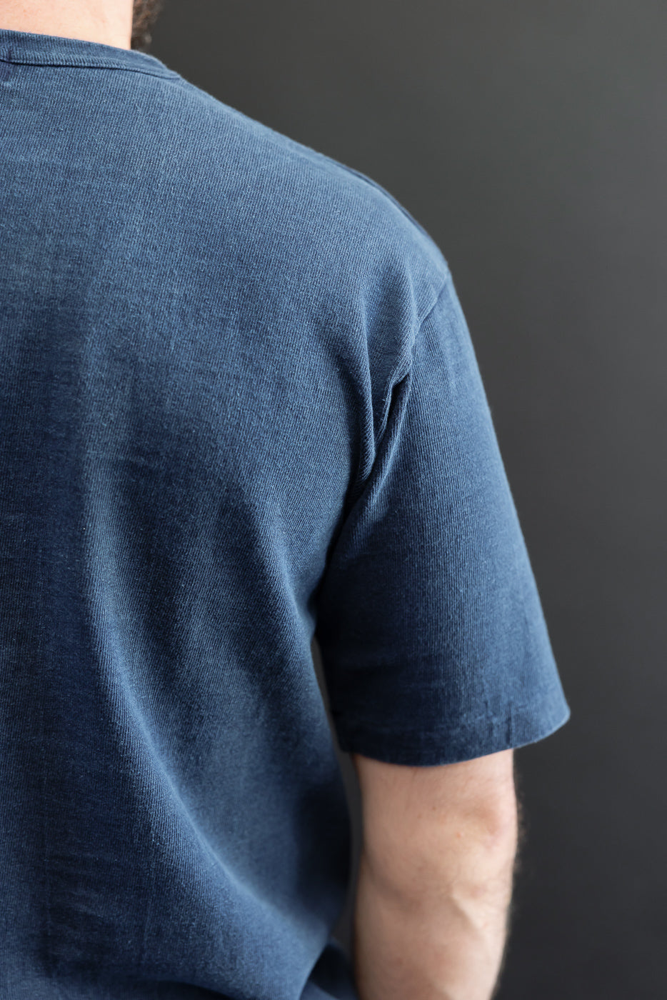 Back view of male model in navy blue t-shirt, showcasing fabric texture and sleeve hem detail.