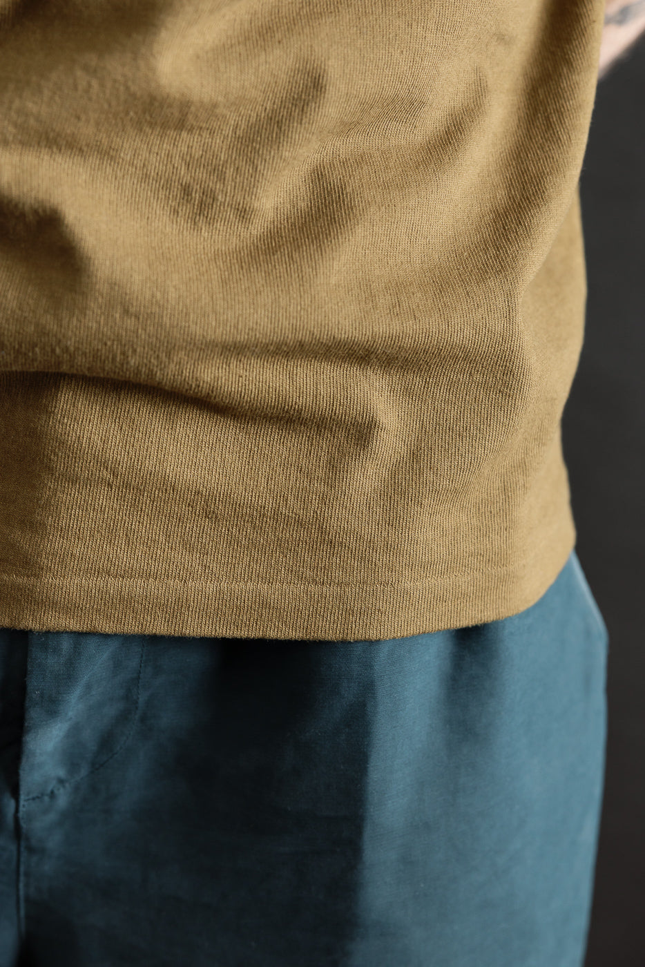 Close-up of khaki heavyweight tee hem, front view, showing fabric texture on male model.
