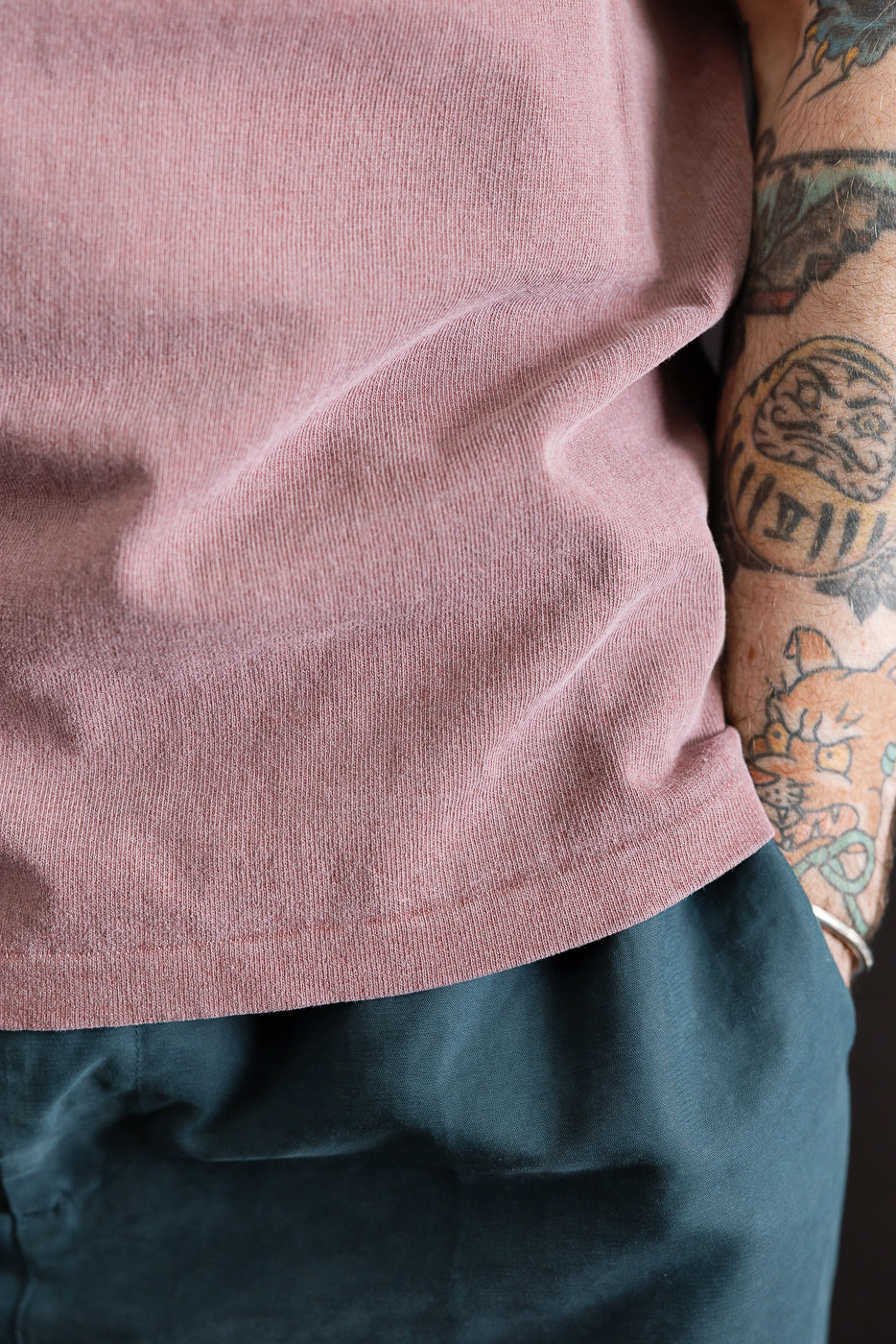 Close-up of male model's front hip in bordeaux pigment-dyed heavyweight tee, showing fabric texture and hem details. Model is 5'9