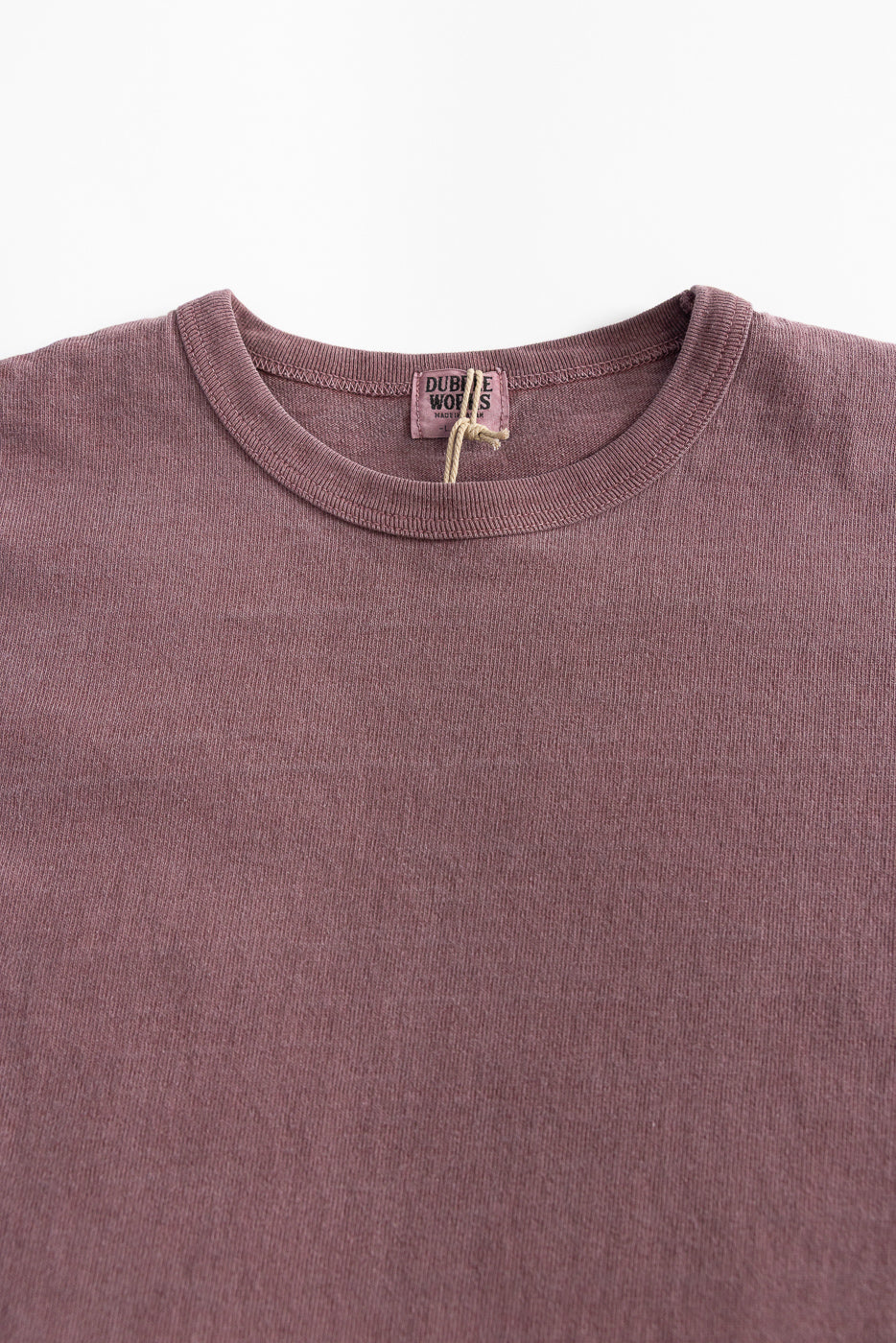 Close-up of front upper chest and collar of heavyweight bordeaux pigment-dyed tee, showing crew neck, fabric texture, and visible neck tag.
