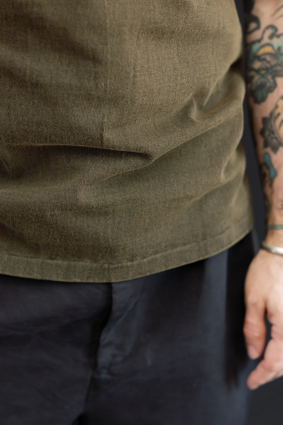 Close-up front view of olive corduroy shirt hem on male model, 5'9