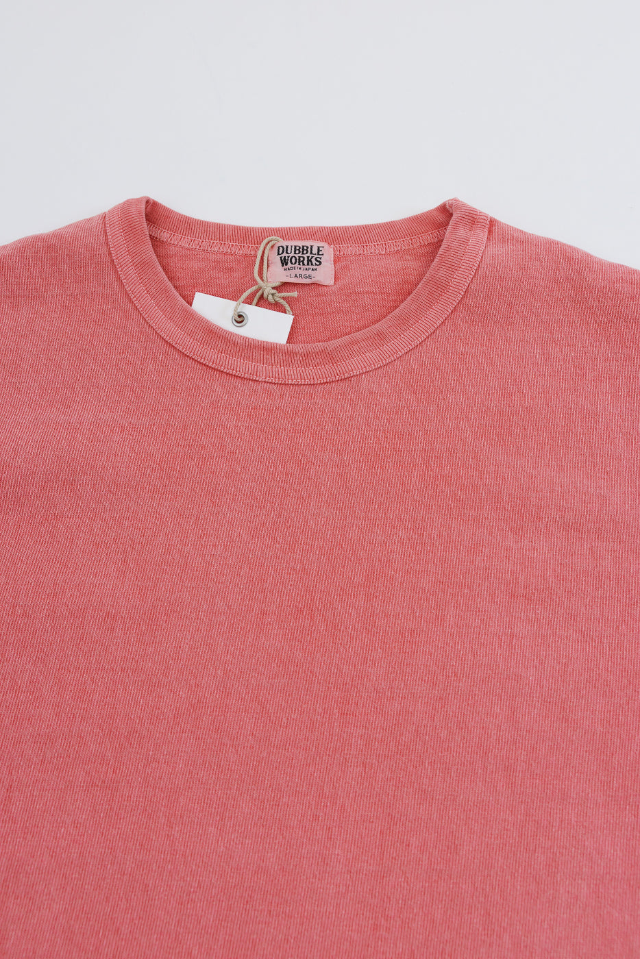 Close-up front view of coral pink crew neck tee, showing Dubble Works tag, ribbed collar, and soft cotton texture