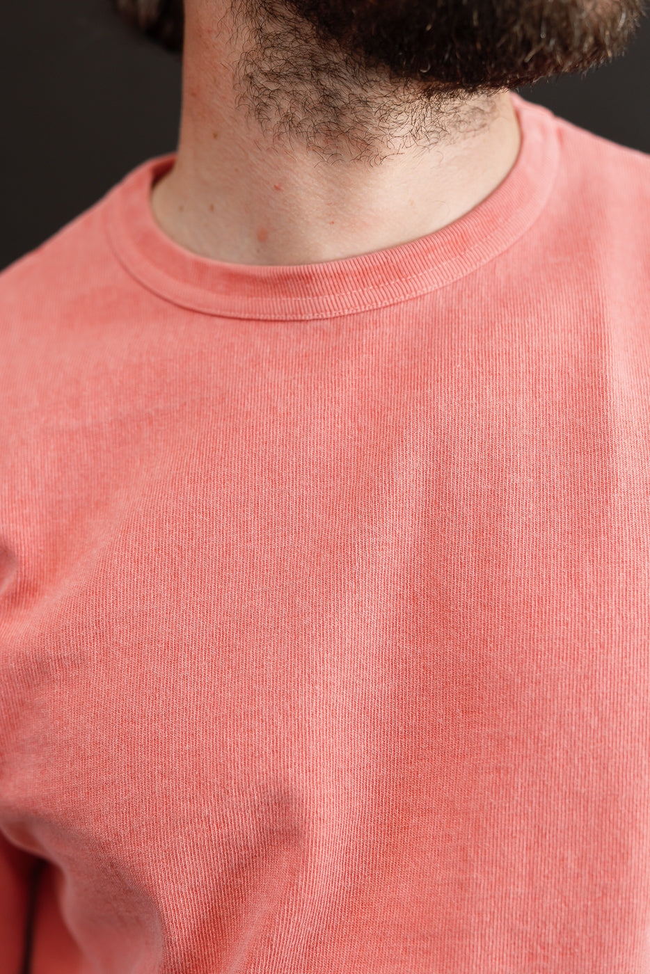 Close-up front view of male model wearing coral crew neck tee, showing ribbed collar and soft cotton texture