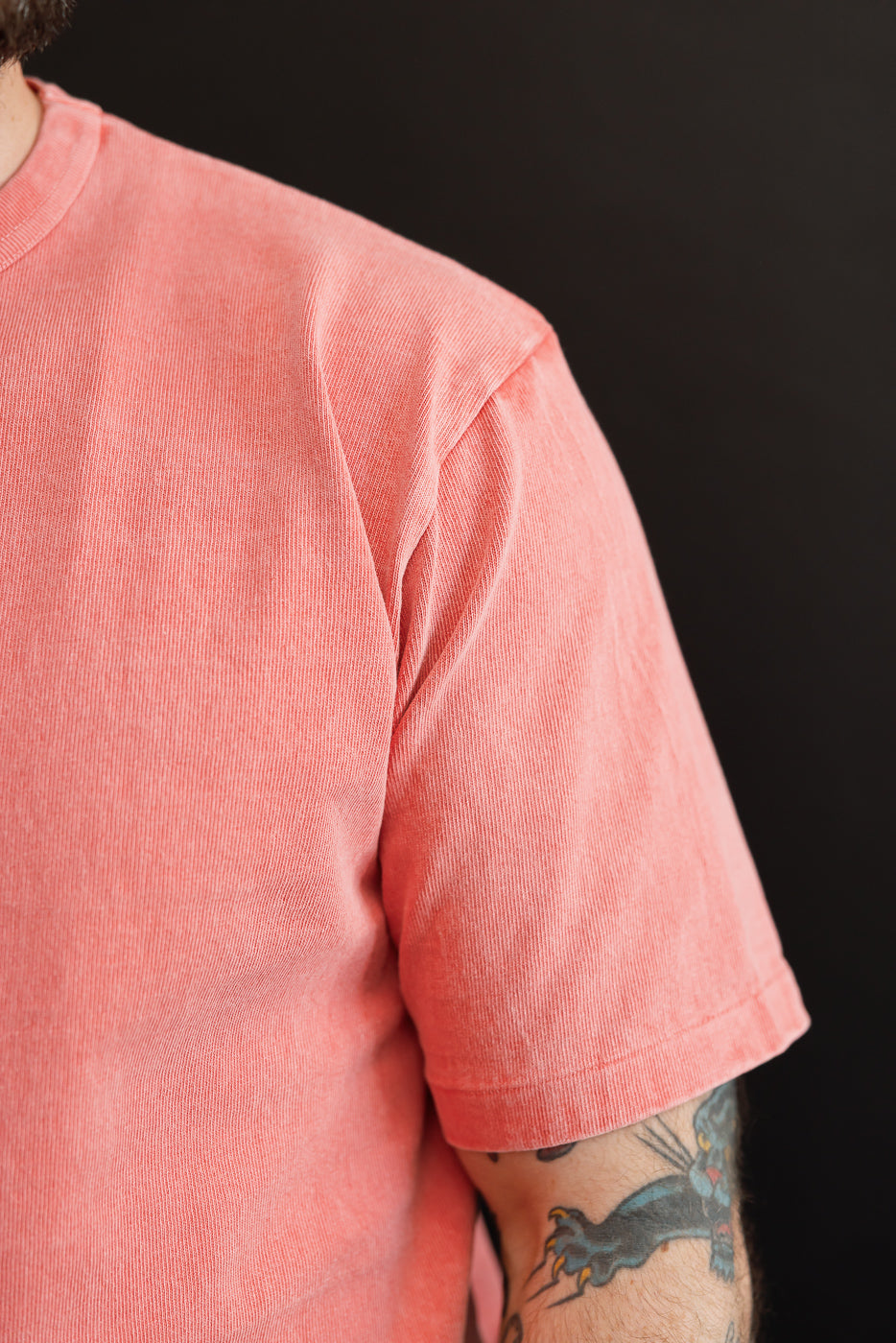 Close-up of male model's shoulder and sleeve, showcasing textured coral t-shirt with ribbed fabric and hem detail.