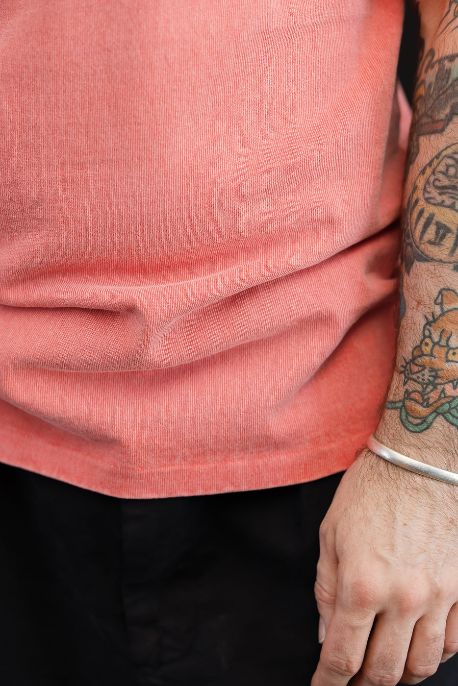 Close-up of male model's torso in coral t-shirt, showing fabric texture and hem detail
