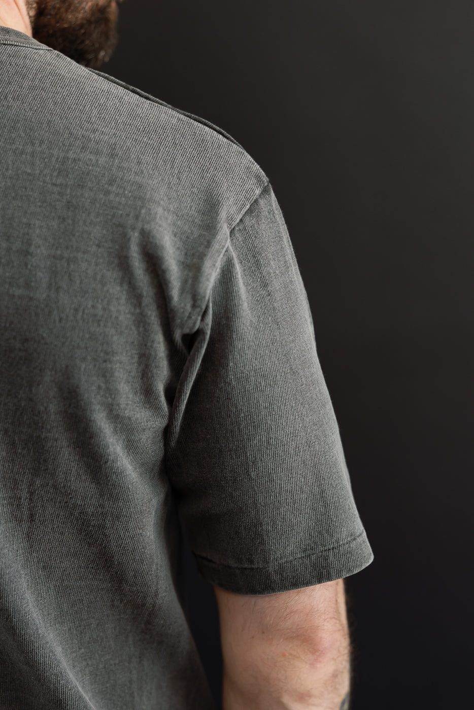 Close-up of male model's shoulder and sleeve, showing textured gray t-shirt fabric and hem detail.