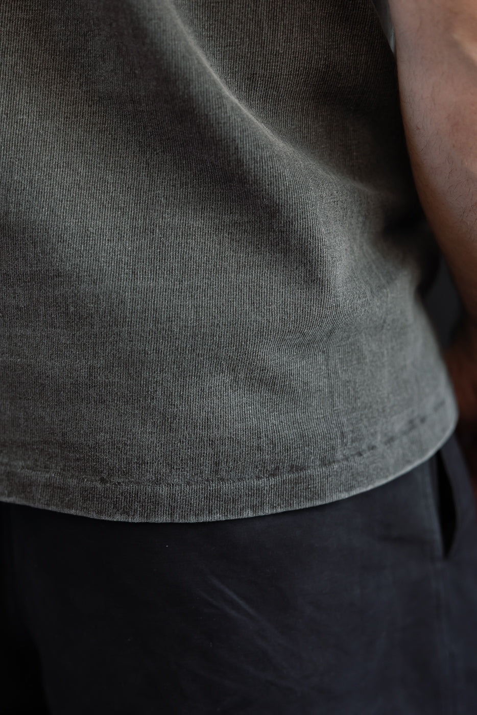 Close-up front view of dark grey ribbed tee hem on male model, 5'9