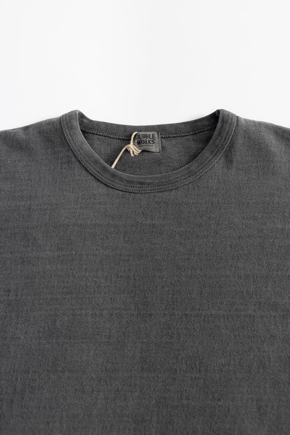 Close-up front view of heavyweight pigment-dyed black tee shirt collar, fabric texture, and tag.