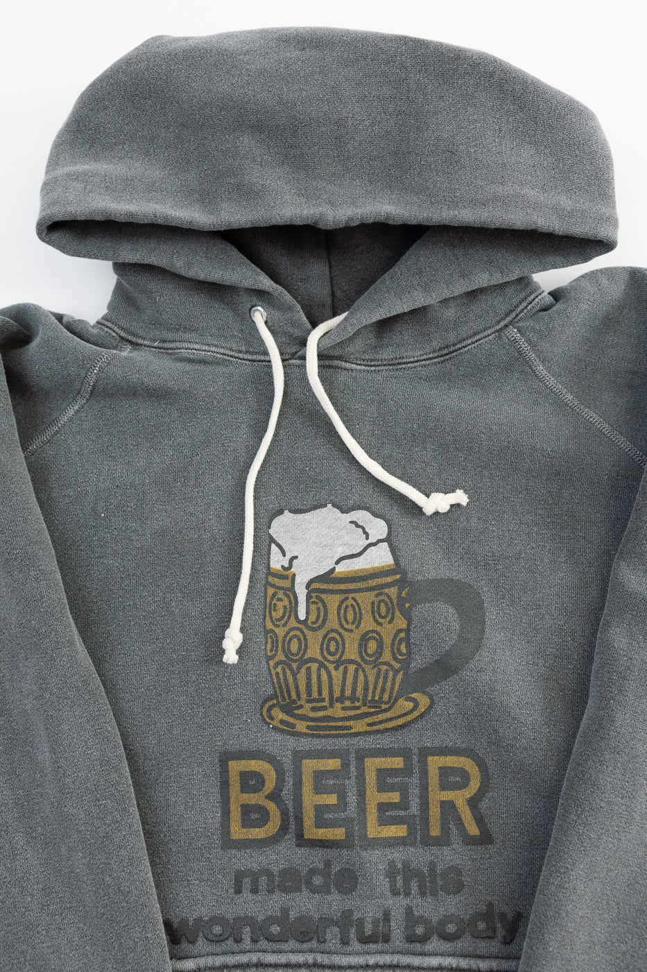 Close-up of front of faded black hoodie with white drawstrings, beer mug print, and chest text details.