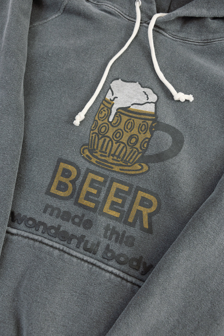 Close-up of front chest graphic on faded print hoodie, showing beer mug and text details.
