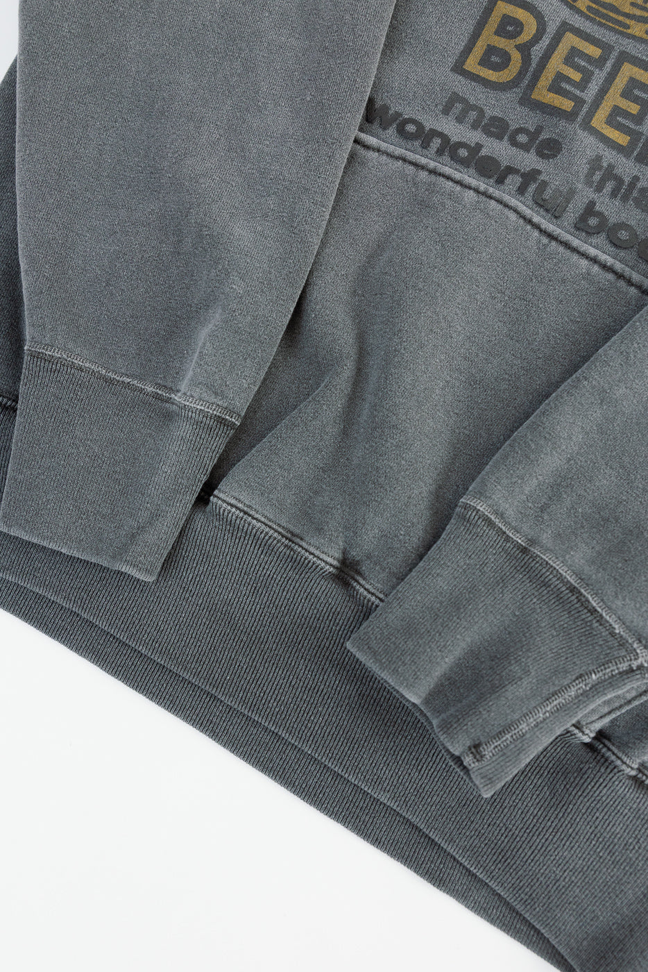 Close-up of front hem and sleeve cuffs on faded print sweat hoodie, showing ribbed texture and partial graphic text.
