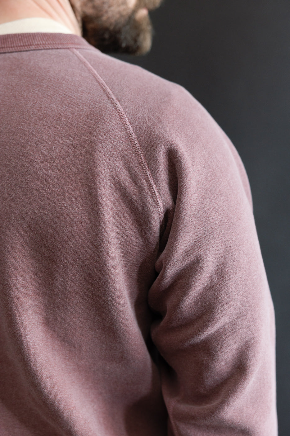 Close-up of male model’s upper back and shoulder in bordeaux sweatshirt, showing fabric texture and raglan sleeve, model is 5'9